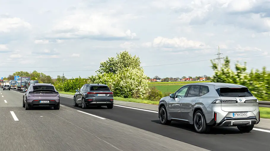 Drei SUVs fahren auf einer mehrspurigen Autobahn. Rechts liegen grüne Felder und Bäume unter einem bewölkten Himmel.