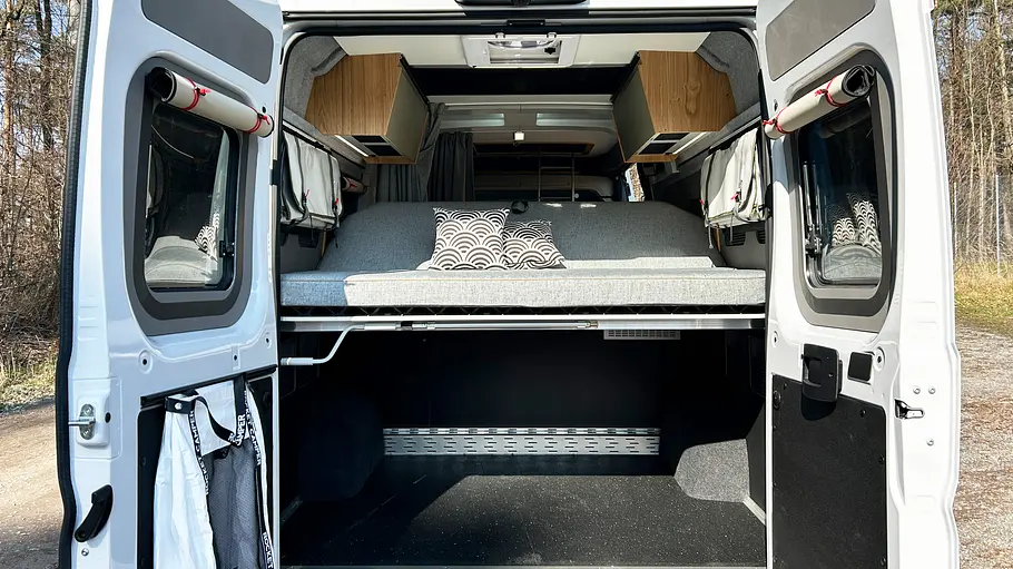 Blick durch die geöffneten Hecktüren auf Heckgarage und Doppelbett im Sofaumbau.