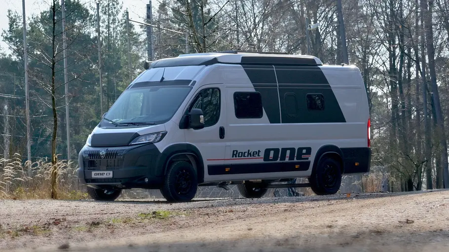 Der Rocket One XL statisch von schräg vorne links auf einem Schotterplatz vor Bäumen.