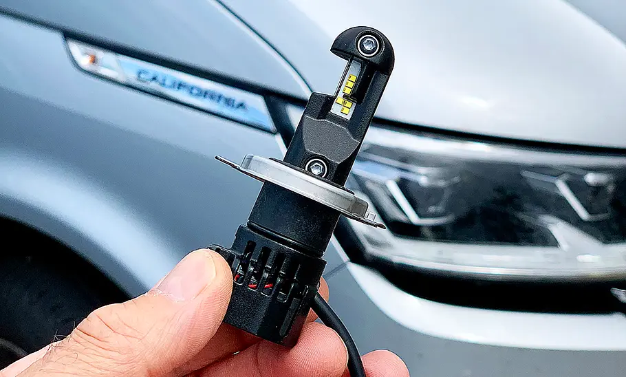 Die Osram H4-LED Birne in der Hand eines Menschen, im Hintergrund sieht man den Ausschnitt eines Autos.