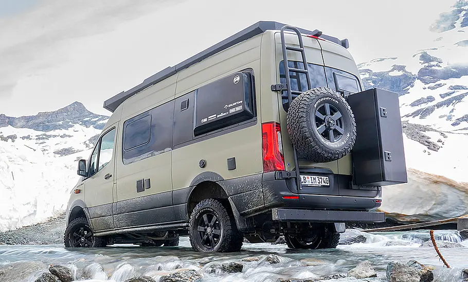 Sam the Van (2025) Sam the Van (2025) stehend, von schräg hinten links. Das Fahrzeug steht mit allen vier Rädern in einem Bergbach, im Hintergrund liegt Schnee.