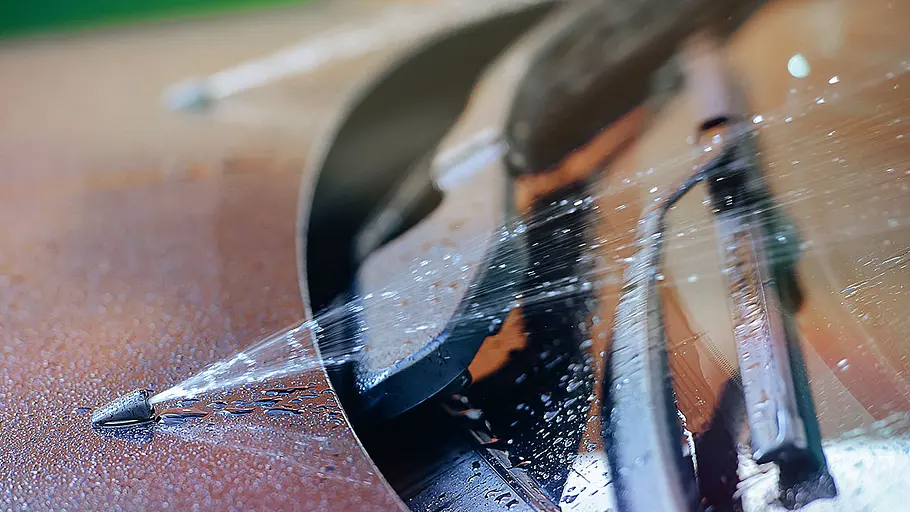 Scheibenwischwasser Das Detailbild zeigt die Scheibenwaschanlage eines roten Autos in Betrieb. Die Düsen spritzen Scheibenwaschwasser auf die Windschutzscheibe.