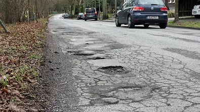 Ein Auto fährt über eine Straße, wo man viele Schlaglöcher sieht. - Foto: Imago
