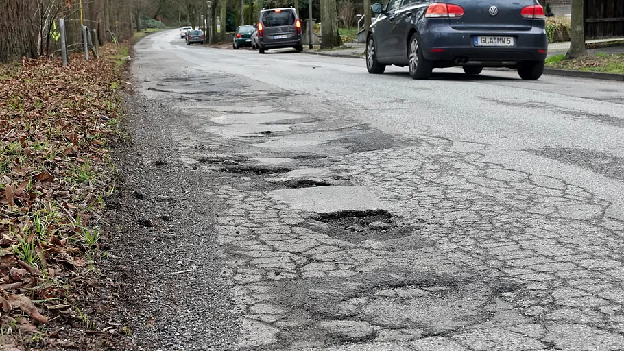 Autos fahren über eine Straße mit vielen Schlaglöchern.