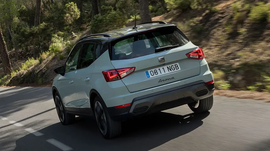 Das Seat Arona Facelift fährt auf einer Landstraße, von hinten links fotografiert.