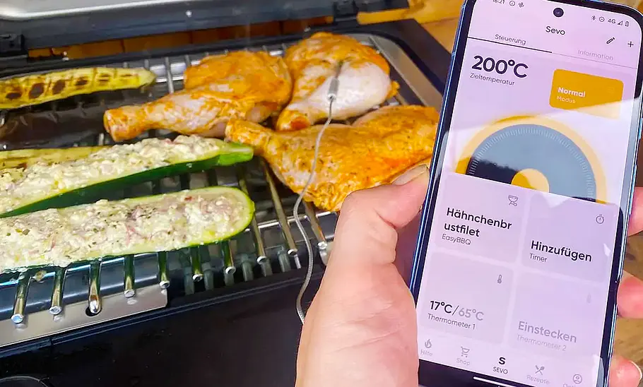 Severin Sevo Smart Control Ein Handy mit geöffneter Severin Sevo Smart Control-App von vorne fotografiert. Im Hintergrund der Grill mit Speisen darauf.