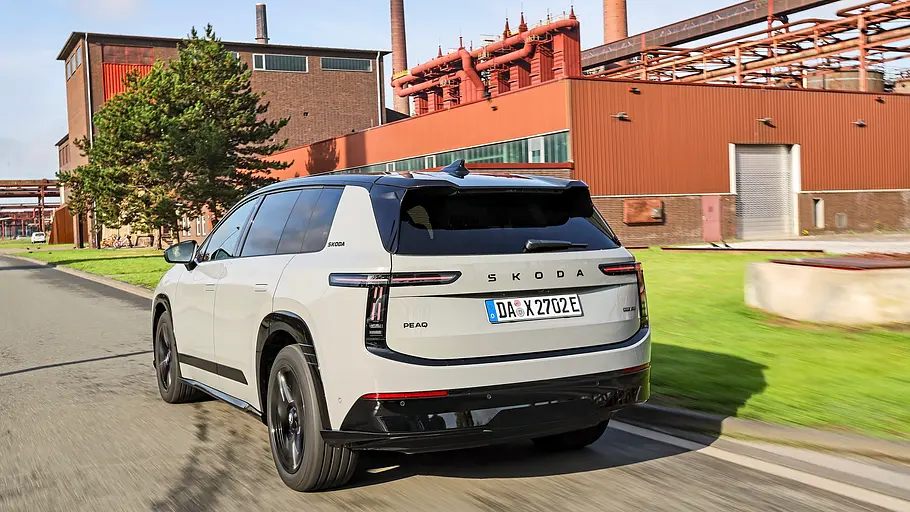 Hellgrauer Skoda Peaq mit schwarzem Dach von schräg hinten, unterwegs vor einer Industriehalle.