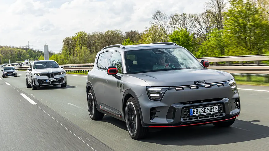 Ein grauer Smart #5 Brabus mit roten Akzenten fährt auf einer Autobahn. Dahinter folgen weitere Autos, am Straßenrand stehen Bäume.
