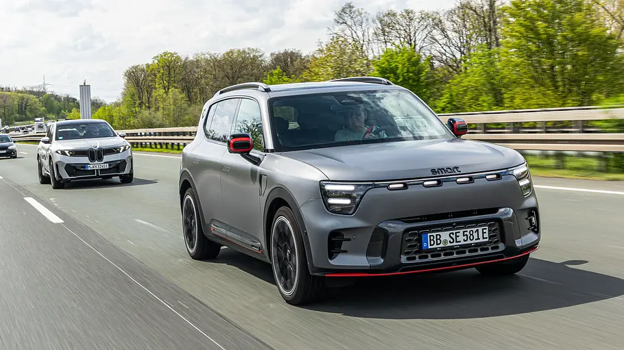Ein grauer Smart #5 Brabus mit roten Akzenten fährt auf einer Autobahn. Dahinter folgen weitere Autos, am Straßenrand stehen Bäume.