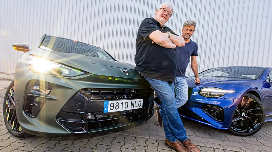 Zwei Menschen stehend vor zwei Autos fotografiert. 