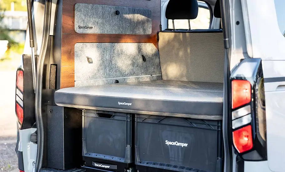 Spacecamper Classic+ Ford (2025) Ein Blick ins Innere des Spacecamper Classic+ Ford (2025) durch die geöffnete Heckklappe zeigt den Schrank und die Stauschubladen unterm Bett.
