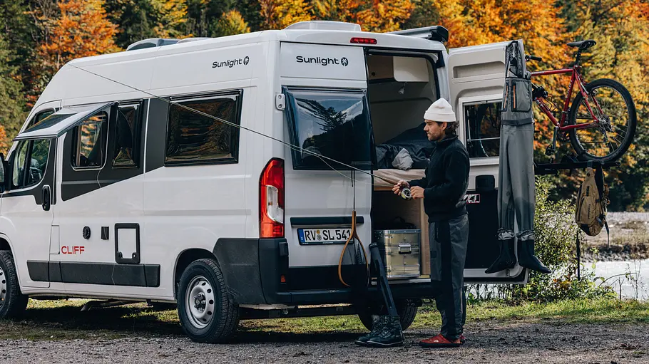 Sunlight Cliff 540 Die Außenaufnahme zeigt den Sunlight Cliff 540 von schräg hinten mit einer offenen Hecktüre. Davor steht ein Mann mit einer Angelroute.