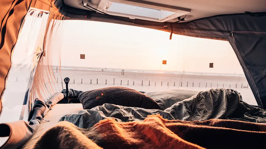 Sunlight Cliff 540V Vanlife Das Schlafdach mit geöffnetem Balg von innen fotografiert. Durch die Öffnung wird der Blick auf einen Strand im Abendlicht freigegeben.