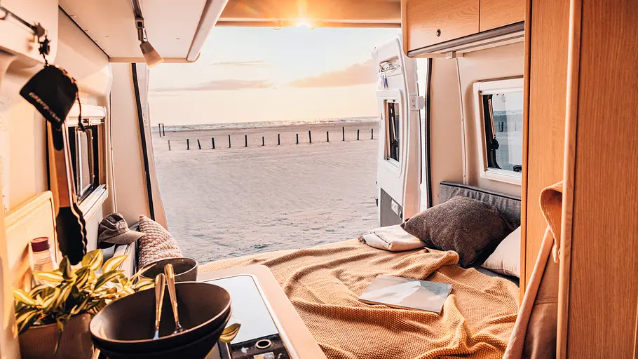 Sunlight Cliff 540V Vanlife Die Hecksitzgruppe im Bettumbau. Die Hecktüren sind geöffnet und geben den Blick auf einen Strand im Abendlicht frei.