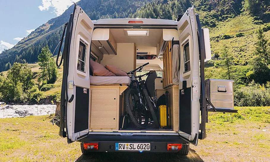 Das Bild zeigt den Heckbereich des Sunlight Cliff Adventure 602 mit geöffneten Hecktüren. Zwei Fahrräder stehen aufrecht im Heck, das Bett ist hochgeklappt.