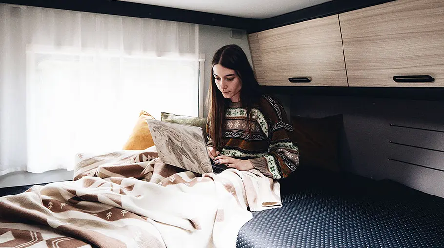 Sunliving S 72 DL Eine Person sitzt mit einem Laptop auf dem Schoß auf einem Einzelbett im Heck des Sunliving S 72 DL.