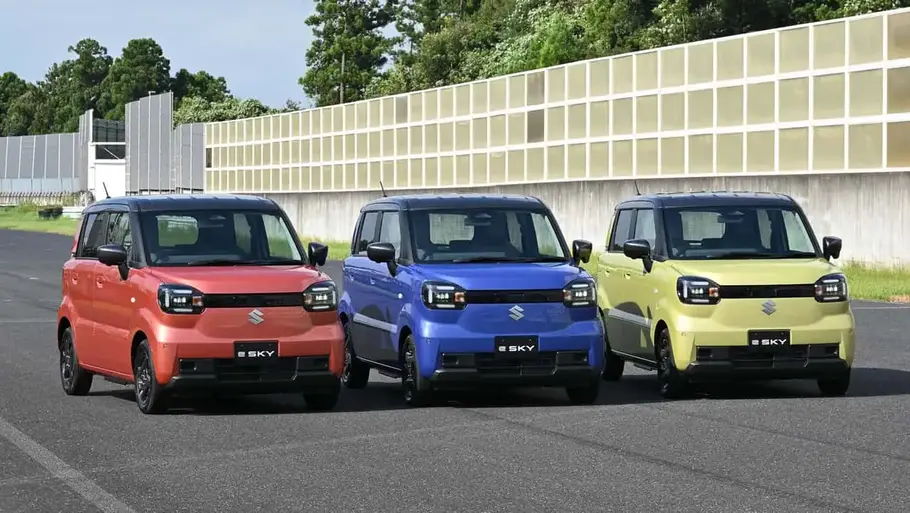 Suzuki e Sky Drei Suzuki e Sky in unterschiedlichen Farben nebeneinander auf einer geteerten Fläche stehend von schräg vorne rechts fotografiert.