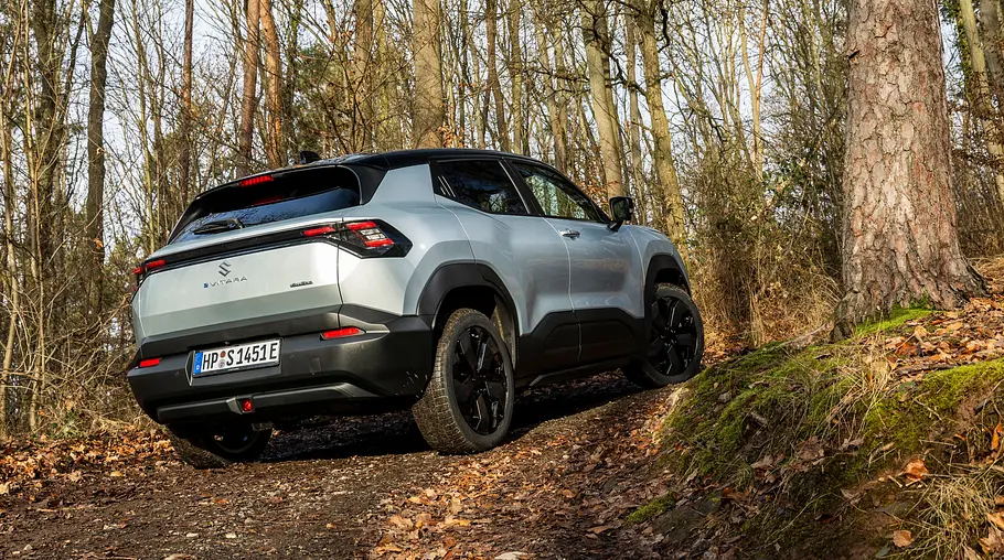 Der Suzuki e Vitara steht in einem Waldstück, von hinten rechts fotografiert.