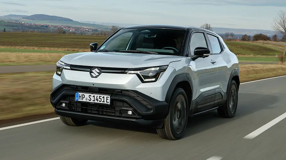 Der Suzuki e Vitara fährt auf einer Landstraße, von vorne links fotografiert.