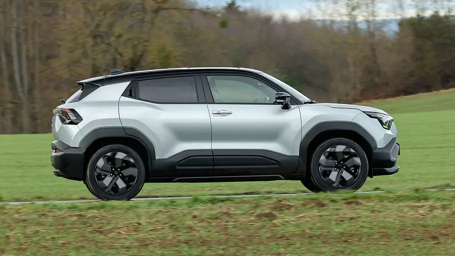 Der Suzuki e Vitara fährt auf einer Landstraße, von rechts fotografiert.