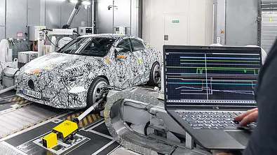 Ein Erlkönig des Mercedes CLA (2025) steht auf dem Prüfstand. Im Vordergrund ist ein Laptop mit Grafiken zu sehen, der von einem Mercedes-Mitarbeiter gehalten wird. - Foto: Mercedes