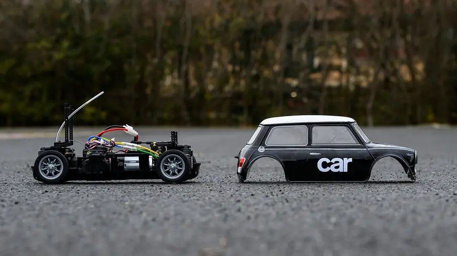 Der Tamiya Mini MB-01 im Test von der Seite. Die Karosserie ist vom Chassis abgenommen und liegt rechts von ihr auf dem Boden.