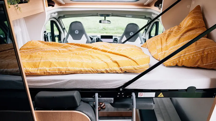 Teilintegrierte Wohnmobile für vier Übersicht Blick auf das ausfaltbare Bett aus der Seitenwand über der Sitzgruppe des Sunlight V67S.