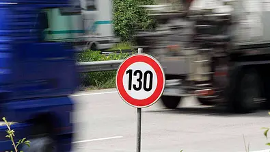Ein Autobahnschild zur 130-km/h-Beschränkung im Vordergrund, vorbeifahrende Fahrzeuge im Hintergrund - Foto: Imago