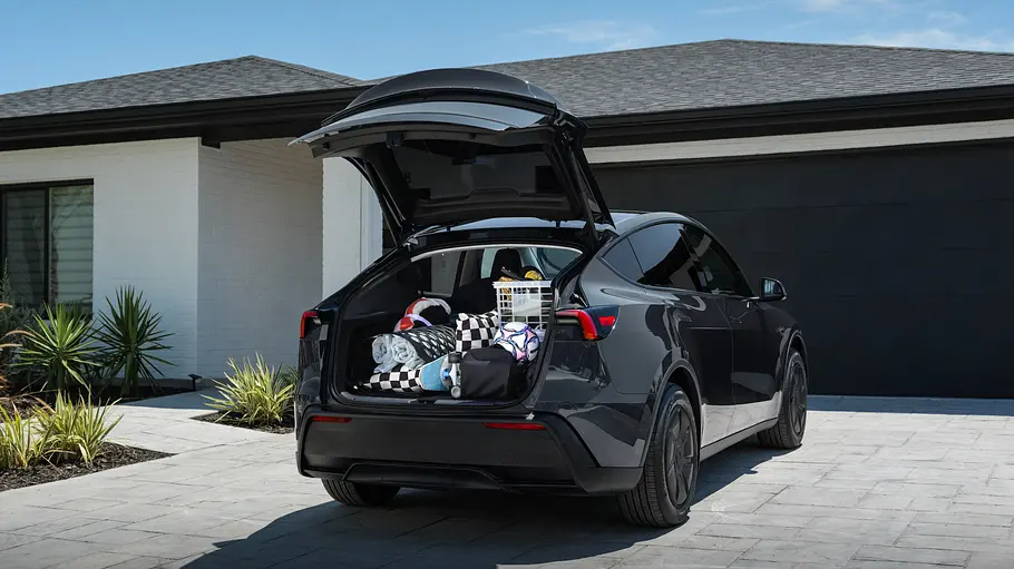 Tesla Model Y Facelift Das Tesla Model Y Facelift steht voll beladen mit offenem Kofferraum vor einem Haus, von hinten fotografiert.