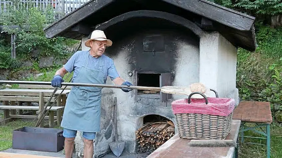 Tirol-Reisereportage im Fendt Bianco Eine Person an einem großen Holzofen, die Kümmelbrot backt.