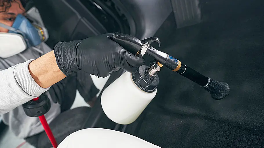 Reinigungspistole Eine Person reinigt den Fußraum eines Autos mit einer Reinigungspistole.