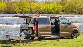 Toyota-Campingzubehör; Toyota Proace Verso, stehend, mit offener Heckklappe und Schiebetüre. Im Van befindet sich eine Campingbox, davor steht ein Tisch mit Klappstühlen. - Foto: Toyota Toyota-Campingzubehör; Toyota Proace Verso, stehend, mit offener Heckklappe und Schiebetüre. Im Van befindet sich eine Campingbox, davor steht ein Tisch mit Klappstühlen. - Foto: Toyota