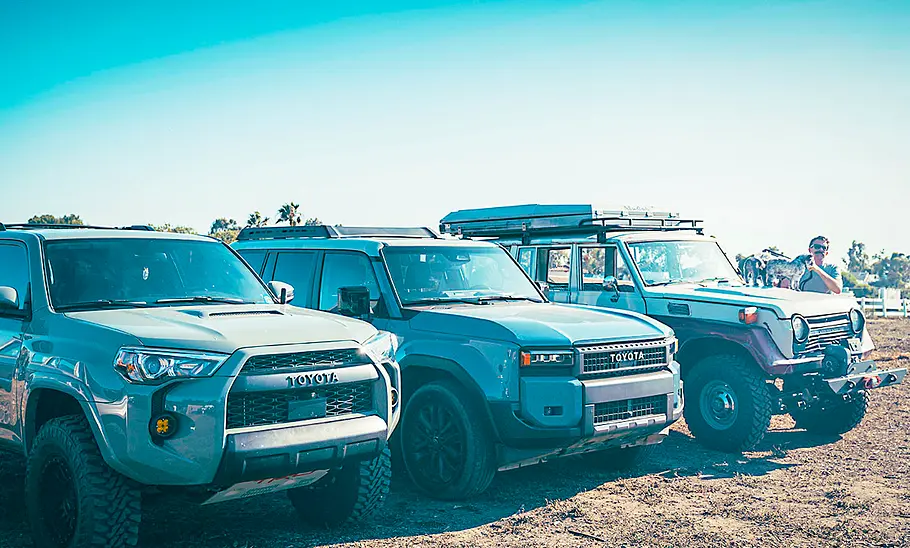Drei Generationen des Toyota Land Cruiser stehend von schräg vorne fotografiert.