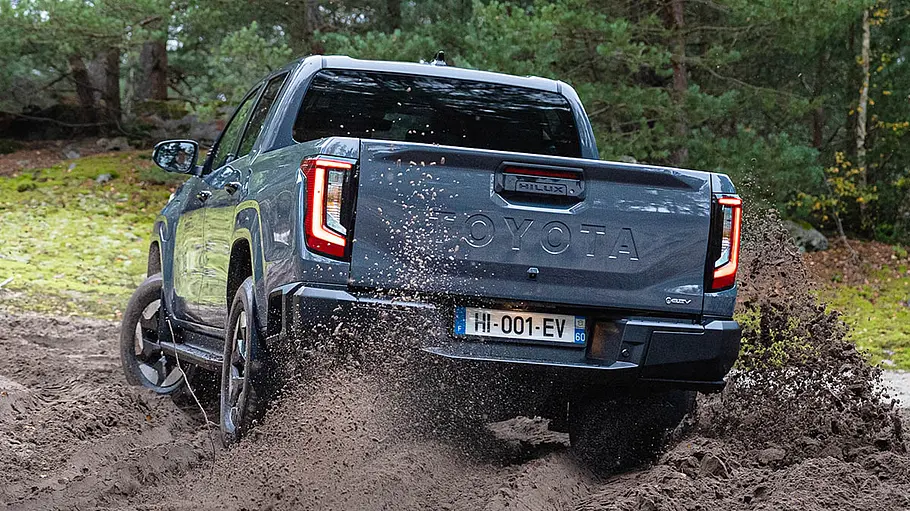 Der Toyota Hilux BEV driftet auf sandigem Boden, von hinten fotografiert.