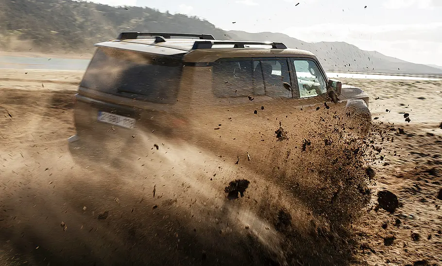 Toyota Land Cruiser (2024) Der Toyota Land Cruiser (2024) fährt eine scharfe Kurve durch Matsch, das hochspritzt; von hinten fotografiert.
