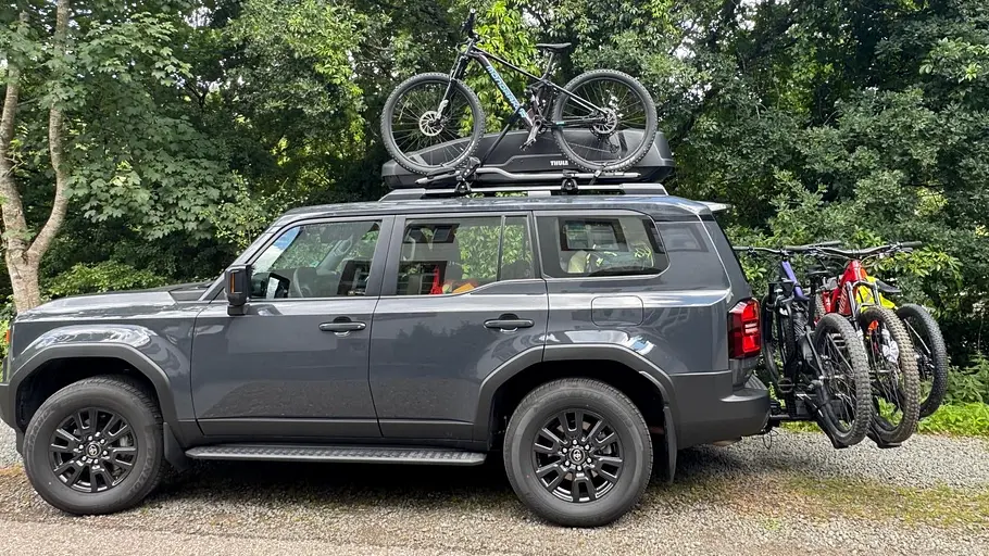 Toyota Land Cruiser Der Toyota Land Cruiser bepackt mit Dachbox, Fahrrad auf dem Dach sowie Fahrrädern auf dem Träger auf der Anhängerkupplung. Fotografiert von der Seite.