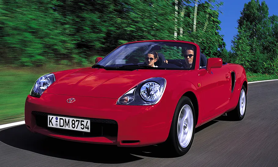 Ein Toyota MR2fahrend auf der Straße mit einem Fahrer sowie einer Beifahrerin.