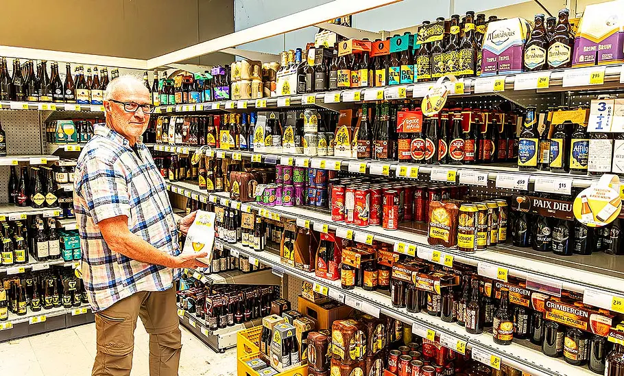 Eine Person steht vor einem gut gefüllten Bierregal im Supermarkt.