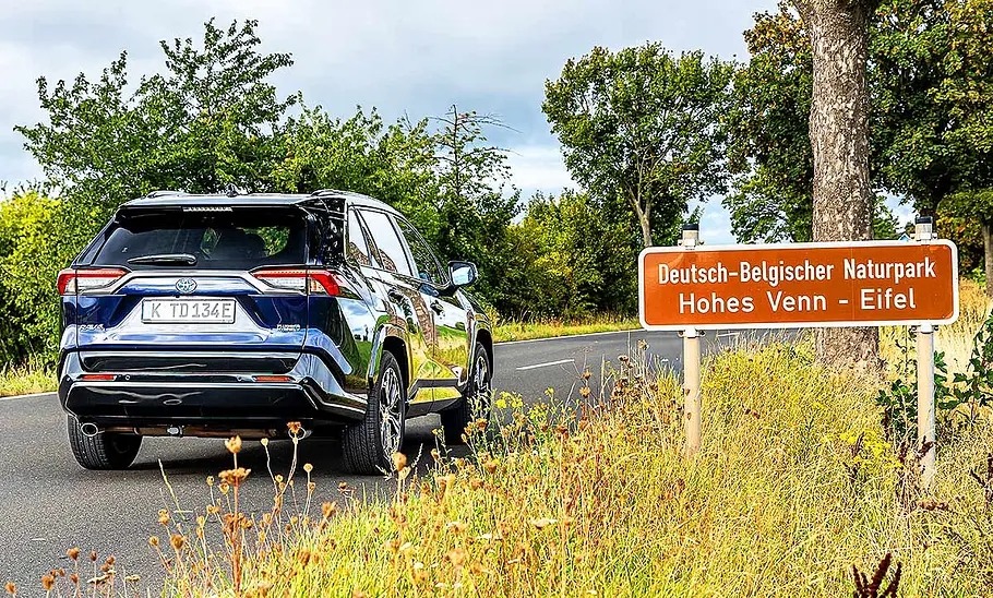 Blick von schräg hinten auf den Toyota RAV4, der auf einer Landstraße entlang fährt.
