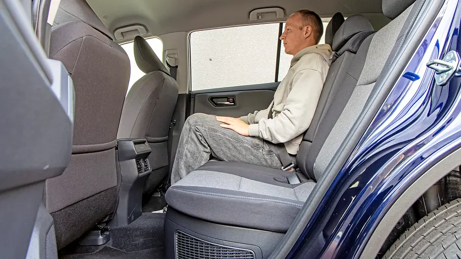 Toyota RAV4 und VW Tiguan im Vergleich Ein Mann in grauem Kapuzenpullover sitzt angeschnallt auf der Rückbank eines Toyota RAV4. Die hintere Tür ist geöffnet.