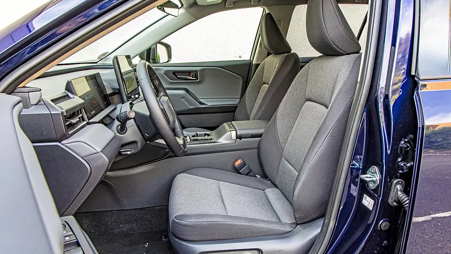 Toyota RAV4 und VW Tiguan im Vergleich Blick durch die offene Fahrertür des Toyota RAV4 auf graue Vordersitze, Lenkrad, Displays und Mittelkonsole eines blauen Autos frei.