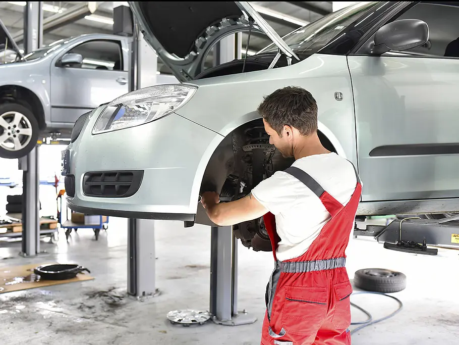Eine Person arbeitet an den Bremsen eines Autos auf der Hebebühne.
