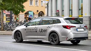 Ein fahrender Toyota Corolla als Uber-Fahrzeug auf einer Straße von schräg hinten. - Foto: Imago