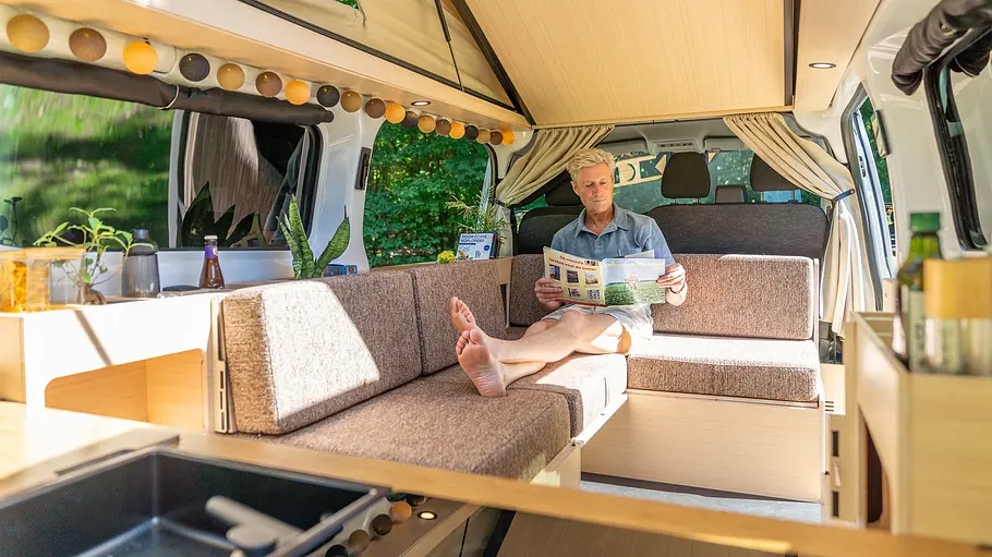 Eine Person entspannt auf dem Längssofa auf der linken Fahrzeugseite im Ventje T7 Camper.