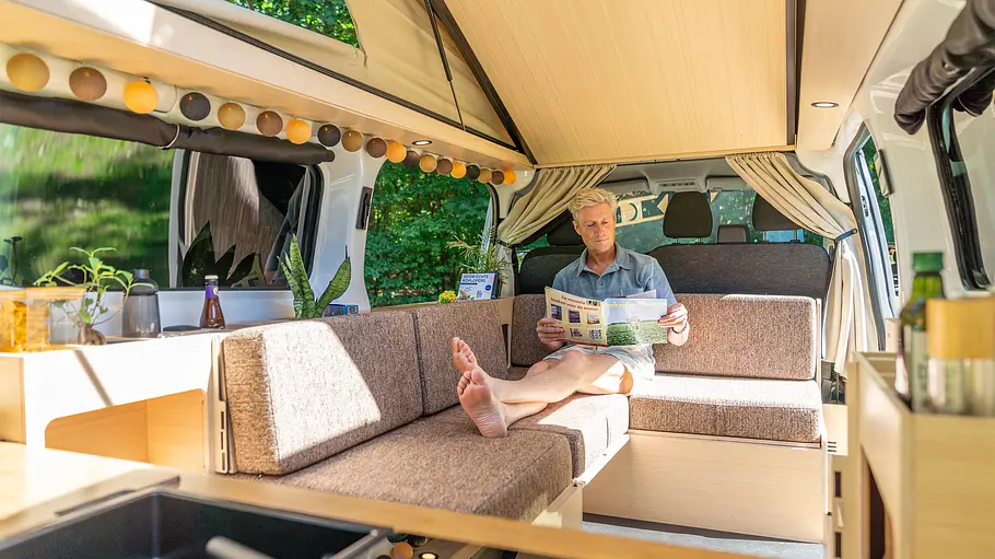 Eine Person entspannt auf dem Längssofa auf der linken Fahrzeugseite im Ventje T7 Camper.