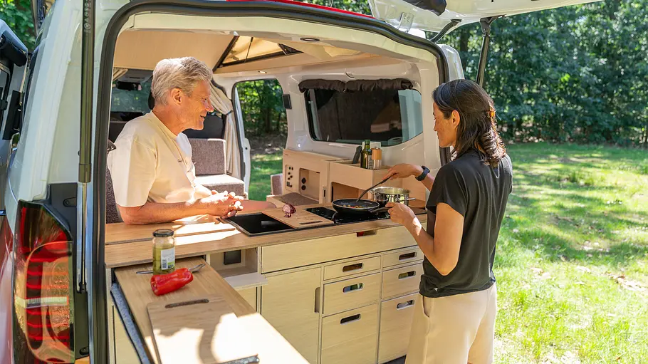 Die Heckküche des Ventje T7 Camper von außen durch die geöffnete Heckklappe fotografiert. Zwei Personen halten sich im Küchenbereich auf.