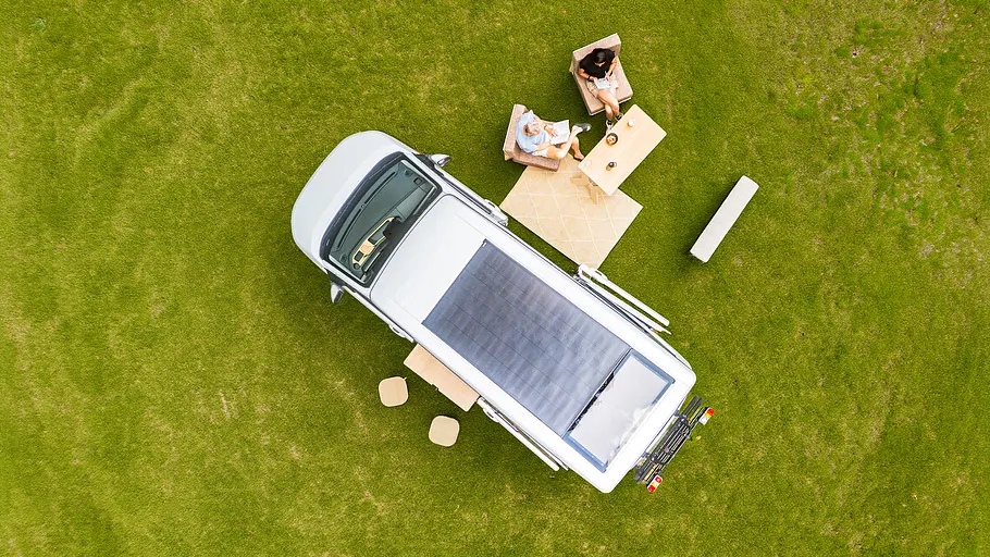 Der Ventje T7 Camper aus der Vogelperspektive, zwei Personen sitzen an einem Campingtisch neben dem Campingfahrzeug.