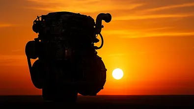 Die Silhouette eines Verbrennungsmotors steht vor einem Horizont, an dem die Sonne untergeht. - Foto: AUTO ZEITUNG (KI-generiert)