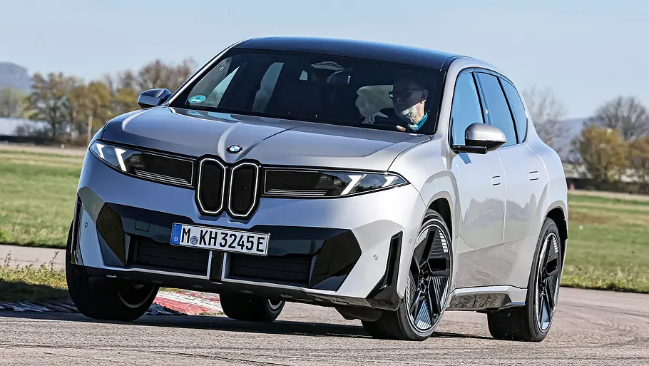Vergleichstest BMW iX3, Polestar 4, Nio EL6 und Smart #5 Ein silberner BMW iX3 fährt auf einer asphaltierten Strecke. Im Hintergrund liegen Wiesen und Bäume.