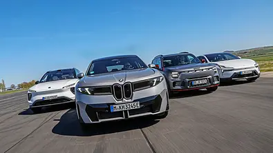 BMW iX3, Polestar 4, Nio EL6 und Smart #5 fahren nebeneinander auf einer breiten Asphaltstrecke. Ein silberner BMW steht im Vordergrund unter blauem Himmel. - Foto: Daniela Loof